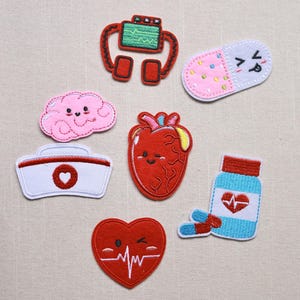 May include: A collection of colorful, embroidered patches with medical themes. Includes a brain, heart, pill, nurse's hat, and a bottle of pills. The patches are in red, pink, blue, and white.