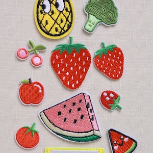 Pode incluir: Uma coleção de patches bordados de frutas e vegetais. Inclui um abacaxi amarelo, brócolis verde, morangos vermelhos, cerejas, uma maçã, uma fatia de melancia, um tomate, uma fatia de limão e uma fatia de melancia sorrindo.