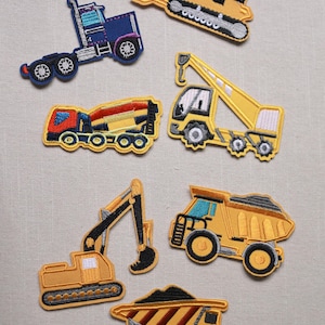 Könnte beinhalten: Gestickte Aufnäher mit verschiedenen Baumaschinen, darunter ein Muldenkipper, ein Bagger und ein Kran. Die Aufnäher sind hauptsächlich gelb, blau und rot, mit schwarzen und weißen Details. Die Aufnäher sind im Cartoon-Stil gestaltet.