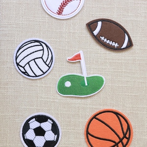 Può includere: Un assortimento di toppe a tema sportivo: baseball, football americano, pallavolo, campo da golf con bandiera, pallone da calcio e basket. Ogni toppa presenta cuciture dettagliate e colori vivaci, perfette per decorare abbigliamento.