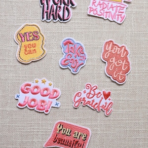 Puede incluir: Una colección de parches bordados con afirmaciones positivas. Los parches presentan frases como «Work Hard», «Radiate Positivity» y «You are Beautiful» en varios colores y fuentes. Ideal para decorar ropa o accesorios.