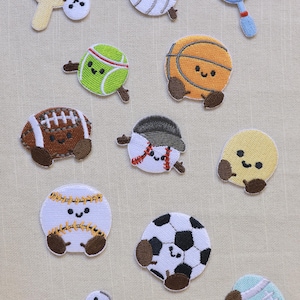 May include: A collection of embroidered patches featuring various sports equipment with smiling faces, including a ping pong paddle, volleyball, tennis racket, tennis ball, basketball, football, baseball, soccer ball, shuttlecock, and skateboard.