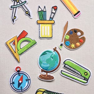 Peut inclure: Ensemble de patchs brodés représentant des fournitures scolaires et artistiques. Comprend un compas, des crayons, une règle, un rapporteur, un globe, une agrafeuse, une palette, un crayon, un pinceau et une gomme.