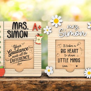 Può includere: Due cornici in legno per l'apprezzamento degli insegnanti. Una cornice ha il testo "MRS. SIMON" e "Your Guidance made all the DIFFERENCE." L'altra dice "It takes a BIG HEART to shape LITTLE MINDS." Entrambe hanno dettagli di mela e margherita.