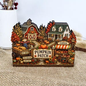 May include: A decorative tabletop display featuring a miniature autumn pumpkin patch scene with a red barn, a house, a scarecrow, and a wagon. The sign reads PUMPKIN PATCH, HAY RIDES, PICK YOUR OWN, and OPEN DAILY, with pumpkins and sunflowers.