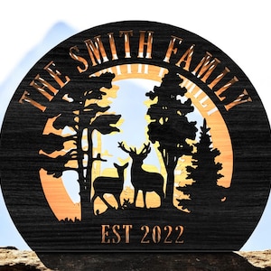 May include: A round wooden sign with the text "THE SMITH FAMILY" and "EST 2022" cut out. The sign features a forest scene with deer and trees. The background is a light orange color.