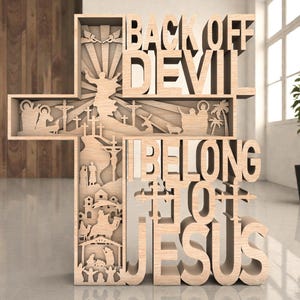 Op de afbeelding: Houten kruisbeeld met de woorden "BACK OFF DEVIL BELONG TO JESUS" in het ontwerp gesneden. Het kruis heeft gelaagde uitsparingen die religieuze scènes en figuren uitbeelden. Het beeld is gemaakt van lichtgekleurd hout.
