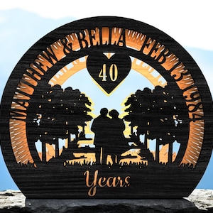 May include: A black wooden anniversary plaque with the names "MATTHEW & BELLA" and date "FEB 13 1984" cut out. The plaque features a silhouette of a couple, trees, and the number "40" inside a heart, with the word "Years" at the bottom.