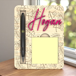 Könnte beinhalten: Schreibtisch-Organizer aus Holz mit tropischem Design, mit einem Stift, einem Notizblock und dem Namen "Hogan" in Pink. Der Organizer hat einen schwarzen Stift und einen gelben Notizblock. Das Design umfasst Ananas, Flamingos und andere tropische Elemente.