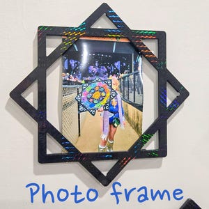 May include: Black star-shaped photo frame with a picture inside. The frame has a holographic design on the edges. The photo shows a person holding a colorful object. The words "Photo frame" are written in blue.