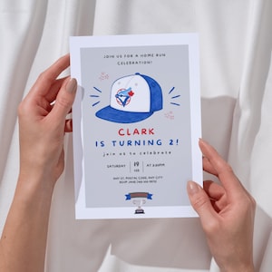 Peut inclure: Une carte d'invitation d'anniversaire rectangulaire sur fond gris clair avec une illustration de casquette de baseball bleue et blanche, le texte JOIN US FOR A HOME RUN CELEBRATION!, CLARK IS TURNING 2!, et les détails du samedi 19 février à 15h30.