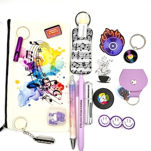 May include: A collection of music-themed accessories including a canvas pouch with watercolor musical notes, a lip balm holder, a purple whistle, a harmonica, two pens, a vinyl record sticker, a purple guitar pick holder, and a triple smiley face pin.
