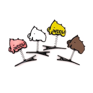 May include: Four hair clips featuring spring-mounted mammoth figures in pink, white, yellow, and brown. The pink and yellow mammoths have the text WOOLI printed on them. Each figure is attached to a black metal alligator-style hair clip.