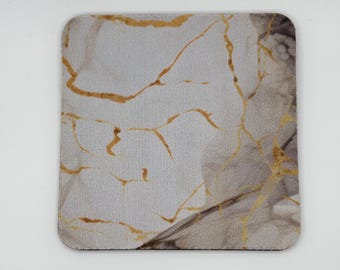 May include: Square coaster with a marble design. The coaster features a light gray background with gold and brown veining. The edges are rounded.