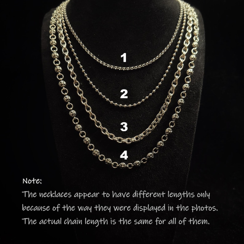 May include: Four silver necklaces displayed on a black stand. The necklaces have different chain styles, including a ball chain and a chain with decorative elements. The image includes text that explains the necklaces appear to have different lengths only because of the way they were displayed.