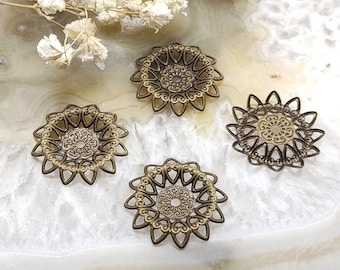 May include: Four antique bronze-colored filigree flower-shaped components. Each component features an intricate openwork design with a central circular pattern and petal-like edges. The components are arranged on a white and gray surface.