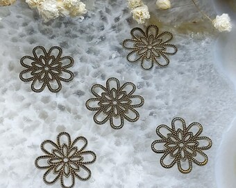 May include: Five bronze-colored filigree flower charms with a detailed openwork design. Each charm features a central circle surrounded by petals, perfect for jewelry making or craft projects. The charms are scattered on a white and gray surface.