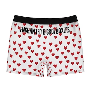 Puede incluir: Bóxers blancos con un estampado de corazones rojos. La cinturilla negra lleva el texto "ENCHANTED BIGBOI BOXERS". Un diseño divertido.