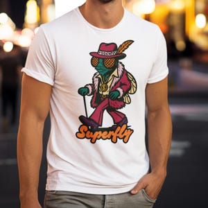 May include: White t-shirt with a cartoon fly character in a burgundy suit, hat, and cane. The fly wears a gold chain, and the word "Superfly" is written in orange script below the image.