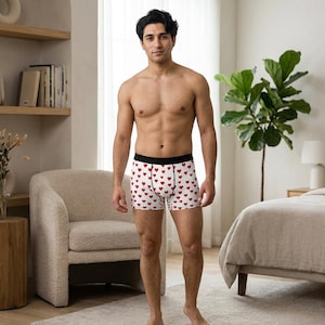 Op de afbeelding: Witte boxershorts met een herhalend patroon van kleine rode hartjes. Het kledingstuk heeft een effen zwarte elastische tailleband en een centrale verticale naad op het voorpand, wat zorgt voor een nauwsluitend silhouet met een klassieke snit.