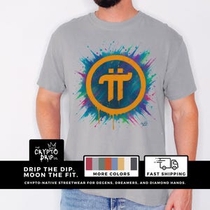 May include: A gray t-shirt with a colorful paint splatter design featuring a yellow circle with a black Pi symbol inside. The text "The Crypto Drip Co." is visible in the bottom left corner.