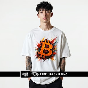 Könnte beinhalten: Weißes T-Shirt mit einem großen, orangefarbenen Bitcoin-Symbol und einem farbenfrohen, abstrakten Explosionsdesign. Das Shirt hat kurze Ärmel und einen Rundhalsausschnitt. Der Text "FREE USA SHIPPING" steht unten.