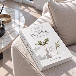 Puede incluir: Un libro de tapa dura titulado The Simple Living London for the love of WHITE YOUR WHITE & NEUTRAL HOME de Christiana Nora. La cubierta blanca presenta una fotografía de tallos verdes con hojas en un jarrón blanco texturizado.