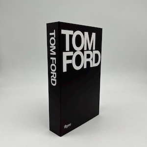 May include: A black book with the words "TOM FORD" in large white capital letters on the front and spine. The book is a hardcover and has the Rizzoli logo at the bottom.