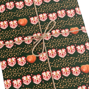 May include: Gift-wrapped package with dark green wrapping paper featuring a repeating pattern of heart-shaped cakes, peaches, and small star-shaped designs. The package is tied with twine.
