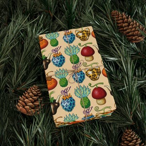 May include: A wrapped gift with a beige background and a repeating pattern of colorful cartoon fruits and objects. The gift is tied with twine and set against a backdrop of pine needles and pine cones.