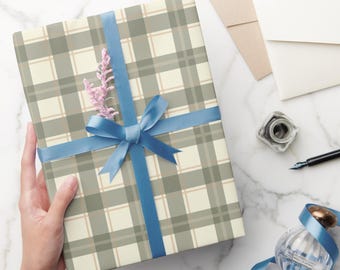 May include: A wrapped gift with a plaid pattern in shades of gray, beige, and tan, tied with a blue ribbon and bow. A sprig of pink flowers adds a delicate touch. Stationery and a perfume bottle are also visible.