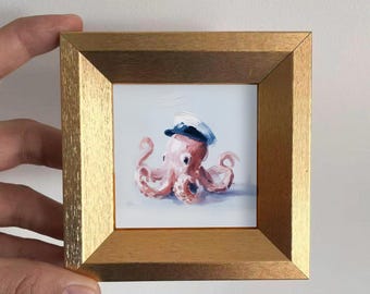 May include: A framed painting of a pink octopus wearing a blue and white sailor hat. The octopus is painted with visible brushstrokes and is set against a light blue background. The frame is a gold color.