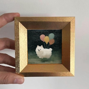 Puede incluir: Pintura enmarcada de un perro blanco y esponjoso sosteniendo globos de colores. La obra de arte está ambientada sobre un fondo verde oscuro y enmarcada en un marco de madera dorada. Los globos son rosas, amarillos y azules.
