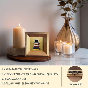 May include: A framed, hand-painted original artwork featuring a stack of books with a coffee cup on top. The artwork is in a gold frame. A lit candle and two glass candle holders with lit candles are also present.