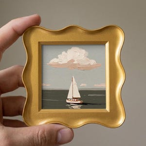 Può includere: Un piccolo dipinto a olio quadrato raffigurante una barca a vela bianca su acqua grigio scuro sotto un cielo grigio pallido con una grande nuvola bianco rosata, racchiuso in una cornice dorata decorativa con bordo ondulato.