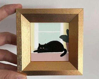 May include: A framed painting depicts a black cat resting on a pink windowsill, gazing forward with yellow eyes. The background shows a window with a light green wall and a potted plant. The frame is a light brown color.