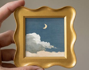 May include: A small square painting in a gold wavy frame featuring a night sky with a crescent moon and a large white cloud. The artwork displays a deep blue background with textured brushstrokes, capturing a serene nocturnal scene.