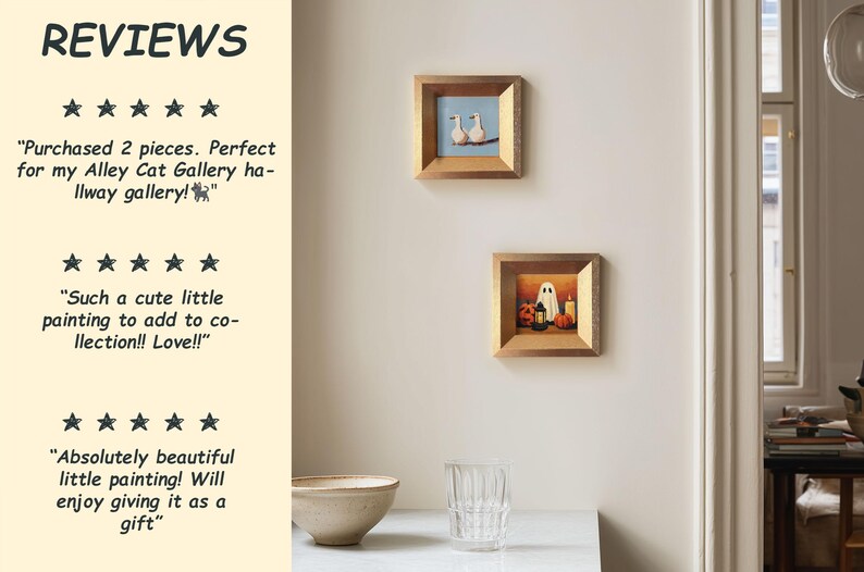 May include: Two small framed paintings are displayed on a wall. One shows two white birds on a branch against a blue sky. The other depicts a ghost, pumpkins, and a candle. The frames are gold-coloured.