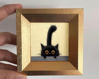Puede incluir: Pintura enmarcada de un gato negro con ojos amarillos asomándose por encima de una repisa gris. El gato tiene una cola y pelaje puntiagudos, sobre un fondo amarillo claro. El marco es de madera con acabado dorado.