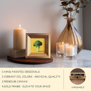 May include: A framed hand-painted original artwork of a broccoli floret on a yellow background. The artwork is in a gold frame. A lit candle and two glass candle holders with lit candles are also in the image. The text in the image says: HAND-PAINTED ORIGINALS, VIBRANT OIL COLORS, PREMIUM CANVAS, GOLD FRAME.