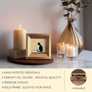 May include: A framed painting of a black and white cat sitting in a window. The painting is in a gold frame and sits on a wooden surface. A lit candle and two glass candle holders with lit candles are also present. The text on the image says "HAND-PAINTED ORIGINALS, VIBRANT OIL COLORS, PREMIUM CANVAS, GOLD FRAME ELEVATE YOUR SPACE."