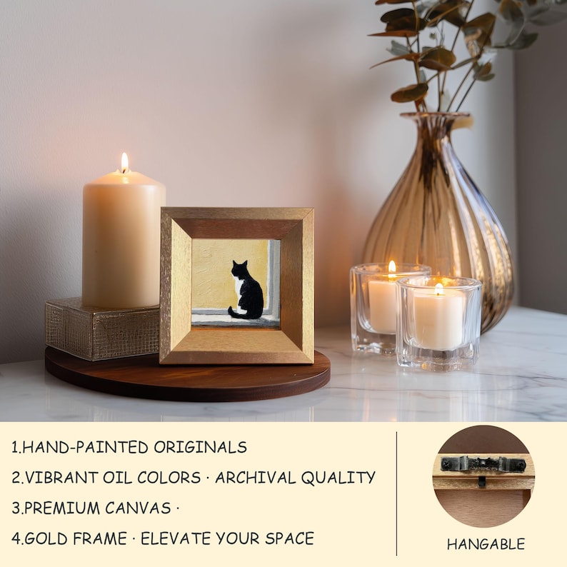May include: A framed painting of a black and white cat sitting in a window. The painting is in a gold frame and sits on a wooden surface. A lit candle and two glass candle holders with lit candles are also present. The text on the image says "HAND-PAINTED ORIGINALS, VIBRANT OIL COLORS, PREMIUM CANVAS, GOLD FRAME ELEVATE YOUR SPACE."