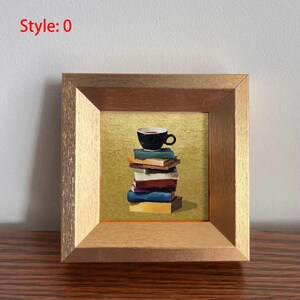 May include: A framed painting depicts a stack of books topped with a black coffee cup. The books are various colors, and the background is gold. The frame is a light brown color, and the text "Style: 0" is in the upper left corner.