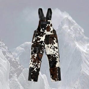 May include: Overalls with a cowhide pattern in shades of brown, black, and white. The overalls have black leather straps and zippers at the ankles. The word "U" is visible on the front pocket.