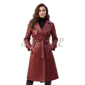 May include: A burgundy leather trench coat with a double-breasted design and a matching belt. The coat features a classic lapel collar and is knee-length. The model is wearing a black turtleneck underneath.