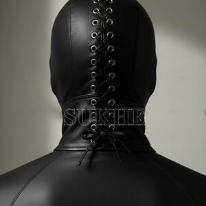 May include: A black leather hood with a lace-up design down the back. The hood covers the head and neck, with the word "SUKHIE" printed on the collar. The hood is part of a leather garment.