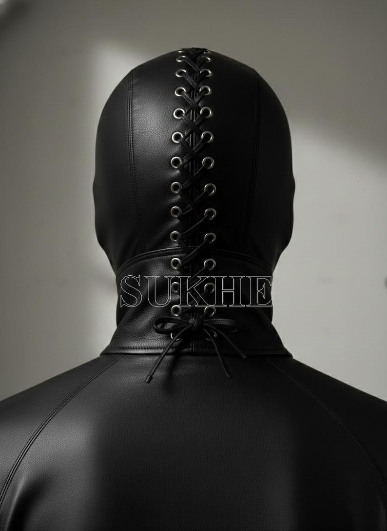 May include: A black leather hood with a lace-up design down the back. The hood covers the head and neck, with the word "SUKHIE" printed on the collar. The hood is part of a leather garment.