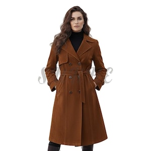 May include: A brown corduroy trench coat with a double-breasted design, a belt, and a classic collar. The coat has a knee-length hemline and is worn over a black roll neck.