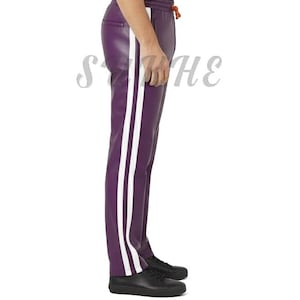 May include: Purple leather pants with two white stripes down the side. The pants have a drawstring waist and are paired with black shoes. The overall style is sporty and modern.