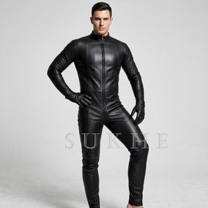 May include: Black leather jumpsuit with a zip-up front, long sleeves, and gloves. The jumpsuit has a stand-up collar and is form-fitting. The word "SUKHE" is visible on the lower part of the jumpsuit.